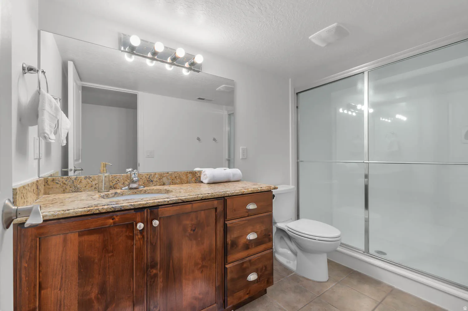 Bathroom featuring a dark wood-finish vanity with a light-toned stone-finish countertop, undermount sink, and a mirrored wall
