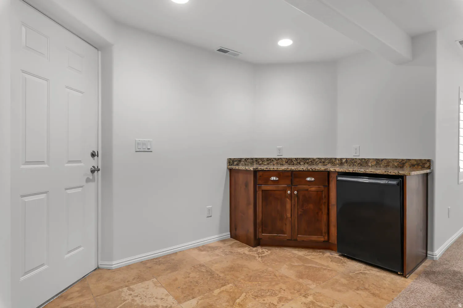 Wet bar featuring wood cabinetry, stone-finish countertop, and under-counter refrigeration