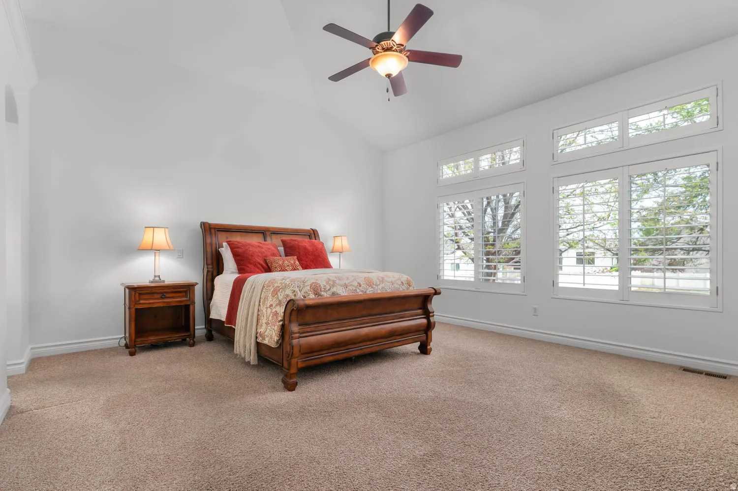 Spacious room featuring vaulted ceilings, plush carpeting, multiple windows with plantation shutters, and a ceiling fan with integrated lighting