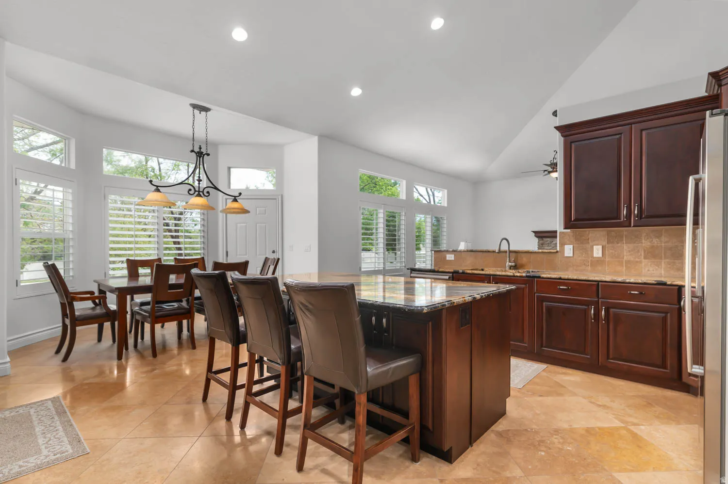 Spacious kitchen and dining area featuring stone tile flooring, dark wood cabinetry, and a central island with countertop seating