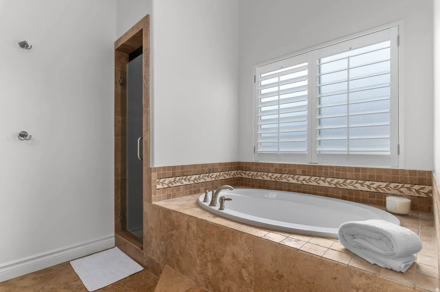 Oval soaking tub with deck-mounted fixtures, surrounded by stone tile and decorative mosaic accents