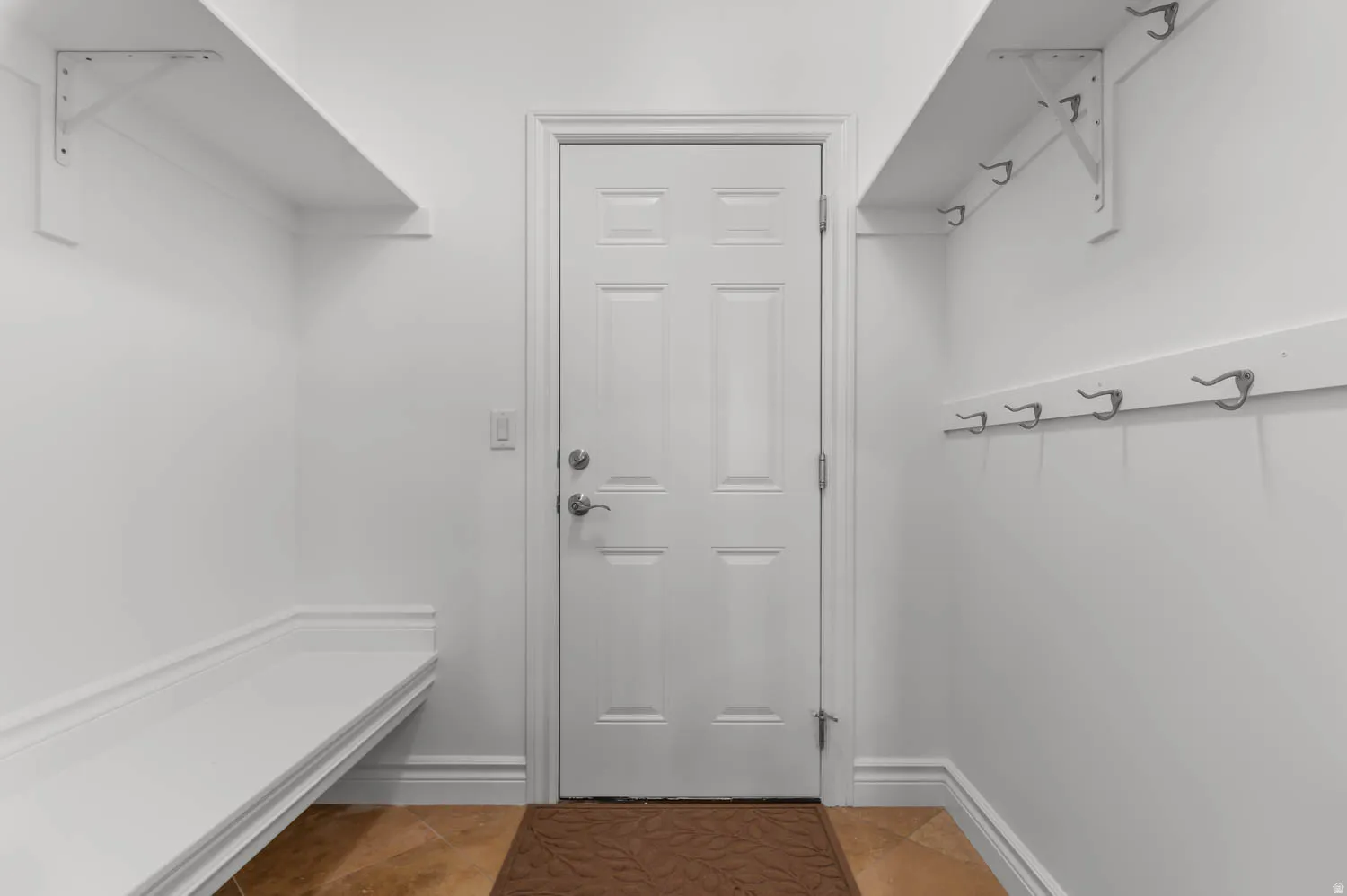 Entryway featuring a paneled door with brushed nickel hardware, built-in bench seating, an upper storage shelf with brackets, a wall-mounted coat rack with multiple hooks, and tile flooring