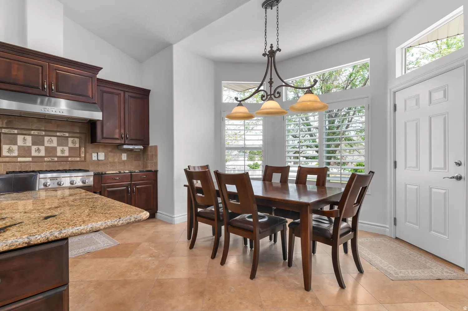 Kitchen and dining area featuring vaulted ceilings, wood cabinetry, stone-look tile flooring, and a stone-look countertop