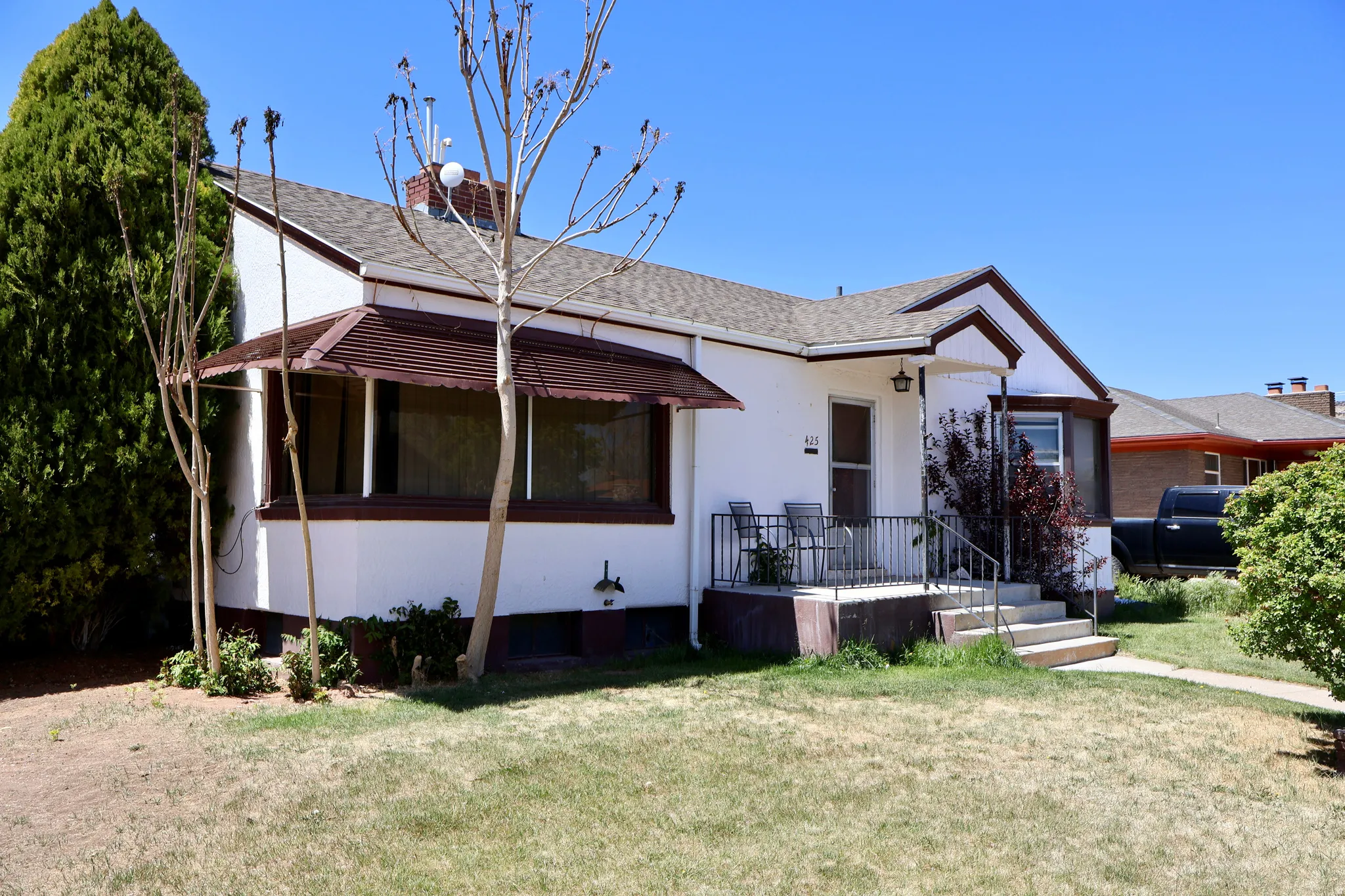 White exterior with brown trim, covered front porch, concrete steps, and a bay window featuring a brown awning
