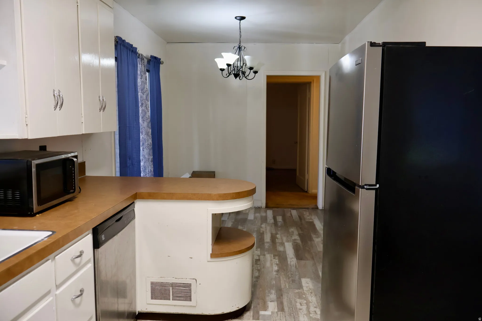 Kitchen area featuring white cabinetry, wood-finish flooring, a stainless steel dishwasher, and a two-tone refrigerator