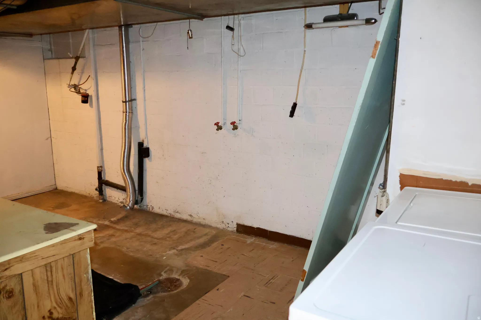 Unfinished basement space featuring a concrete floor, painted cinder block walls, and exposed utility piping