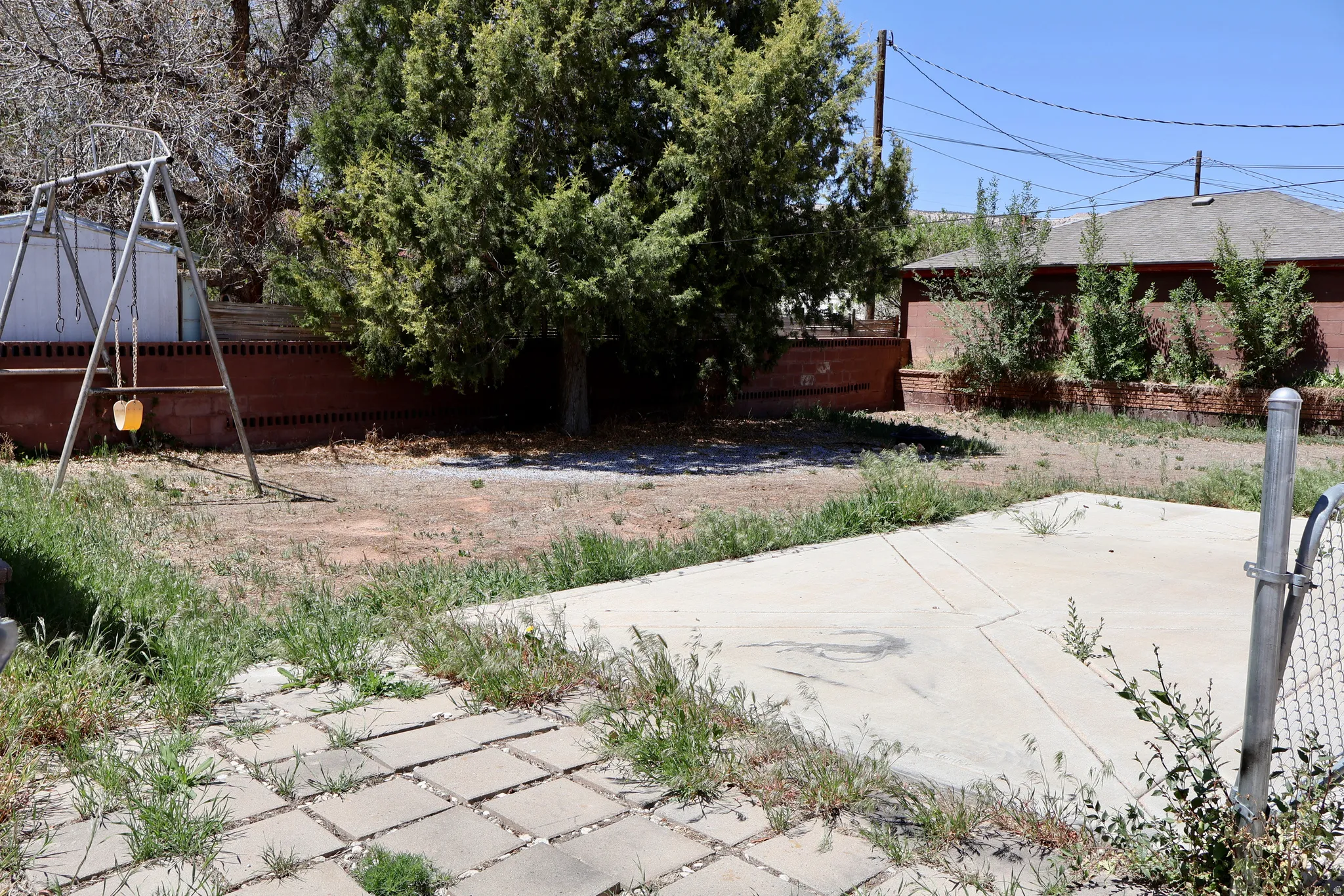 Spacious rear yard featuring a concrete patio, additional paver patio, brick retaining wall, and mature trees