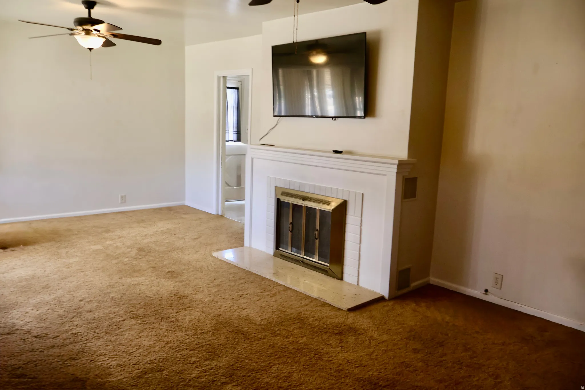 Living area featuring a white mantel fireplace with a brass firebox, a light-toned hearth, and two ceiling fans with integrated lighting