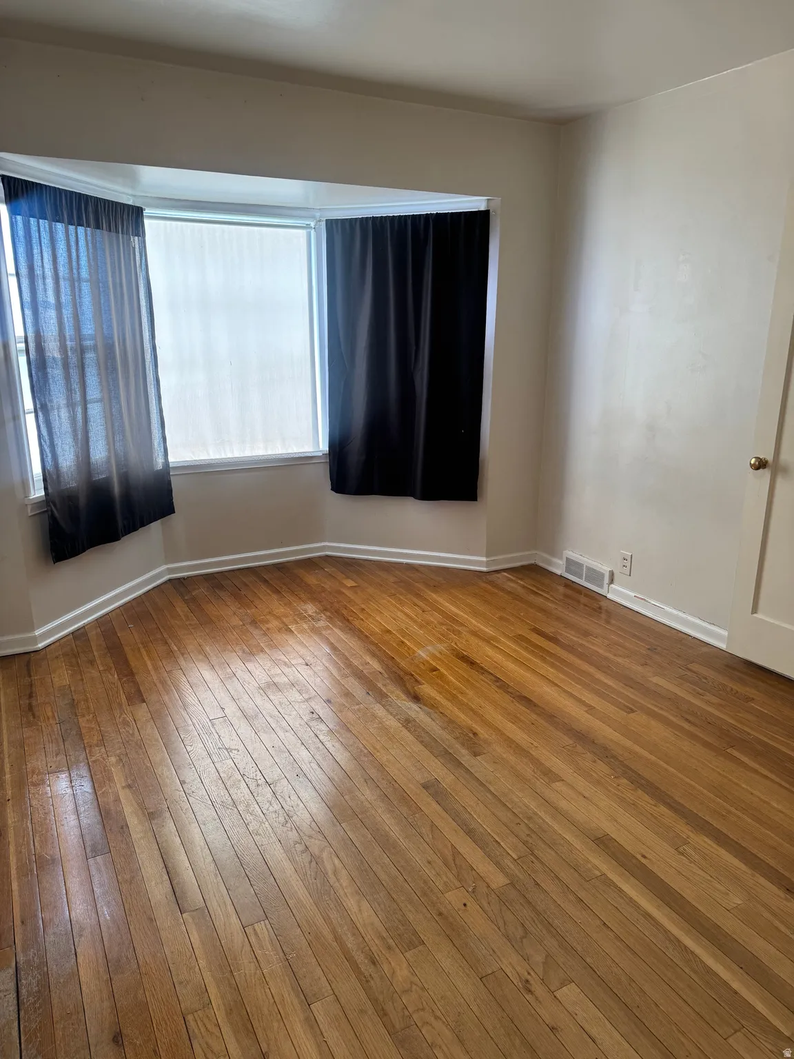 Hardwood flooring throughout, featuring a bay window with natural light
