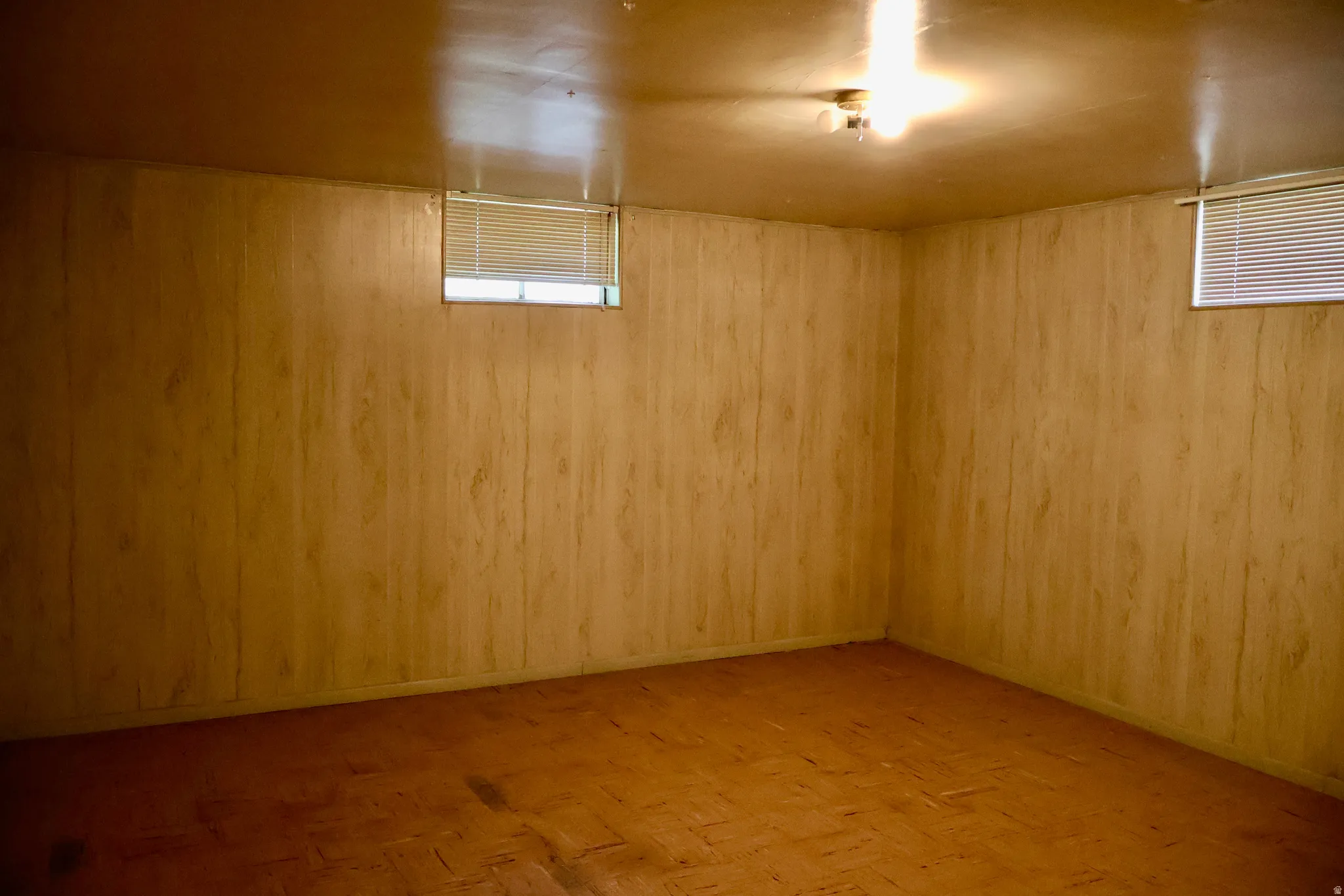 Room featuring wood-finish paneling, two windows with blinds, a ceiling-mounted light fixture, and tile flooring