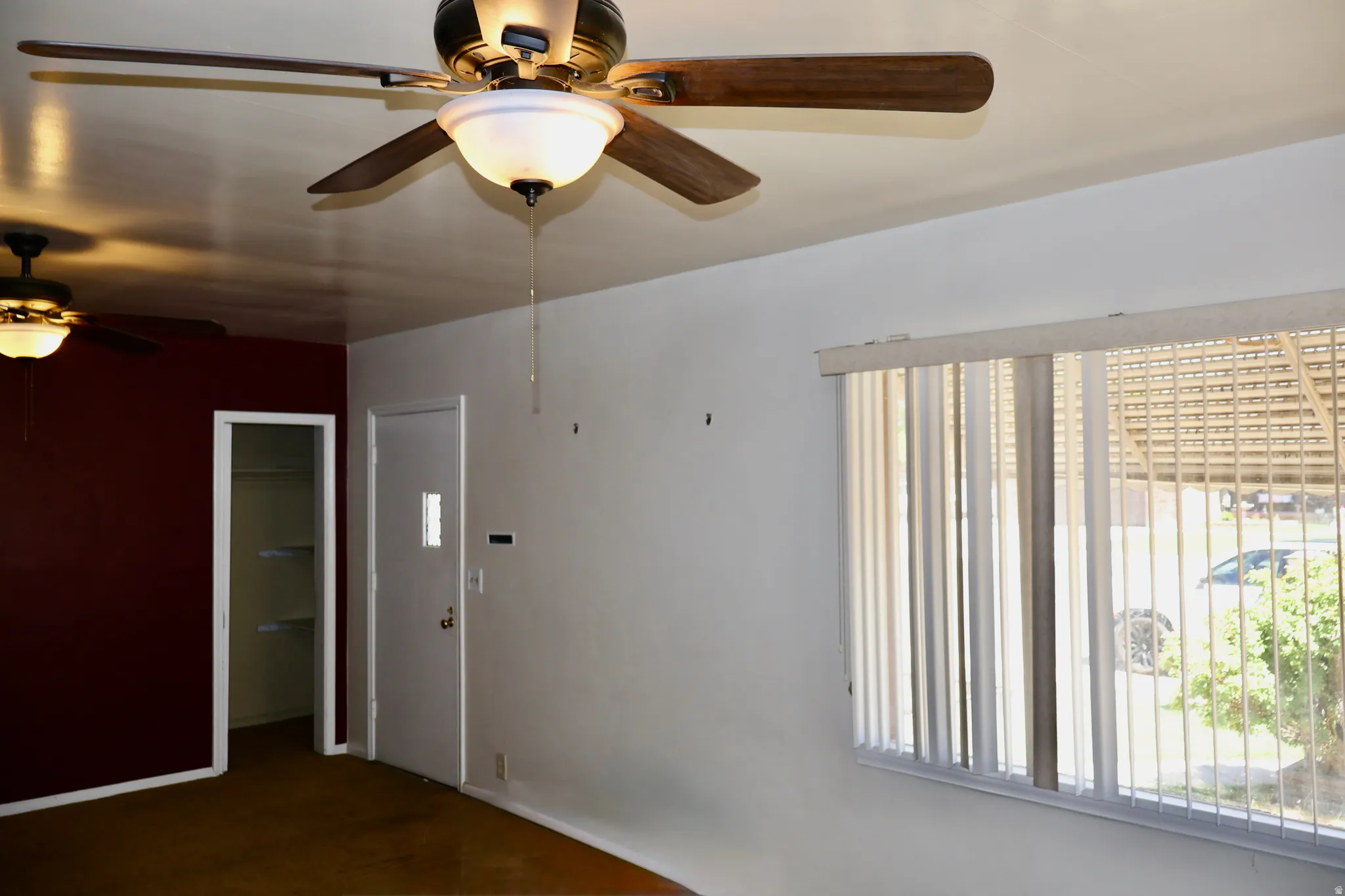 Interior room featuring multiple ceiling fans with integrated lighting, a contrasting accent wall, and a window with vertical blinds