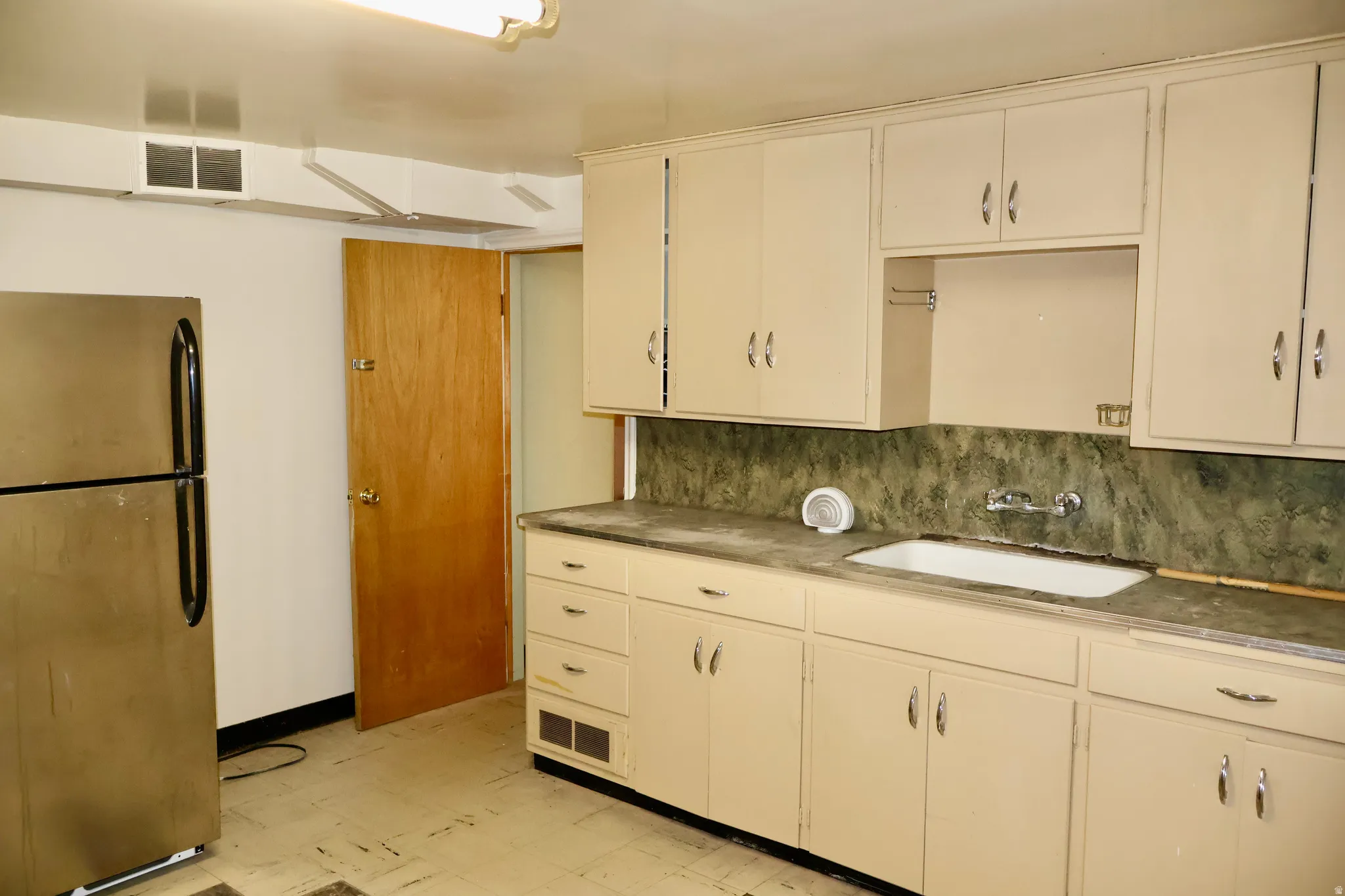 Kitchen featuring cream-colored cabinetry, a built-in sink, and a dark green countertop with matching backsplash