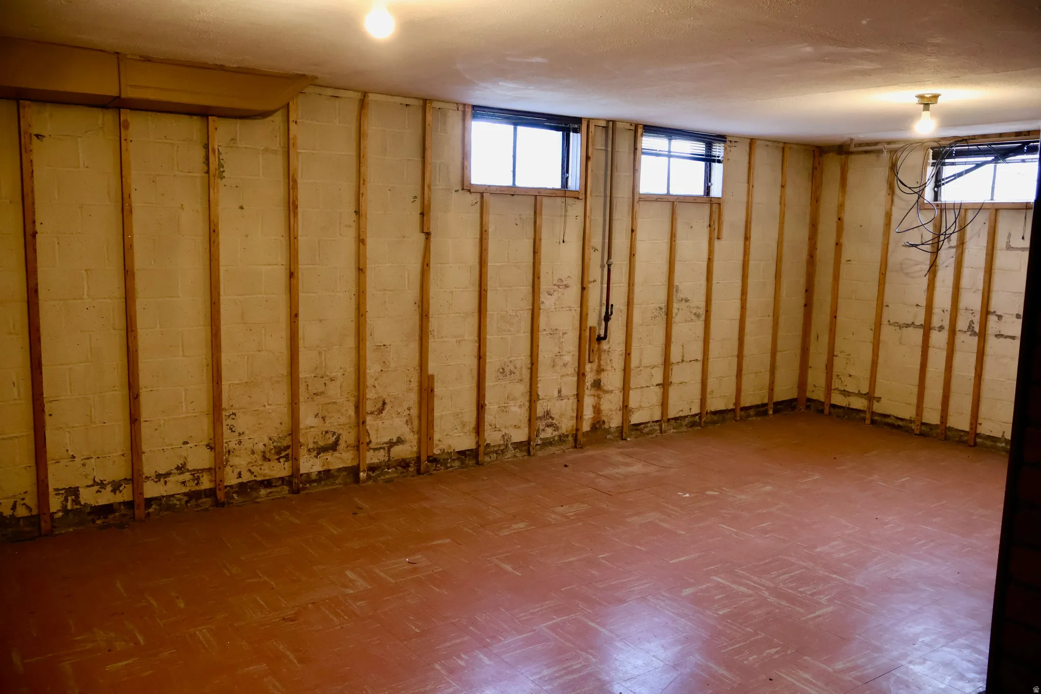 Spacious lower-level room featuring block walls with wood framing, multiple windows, and a tile-patterned floor