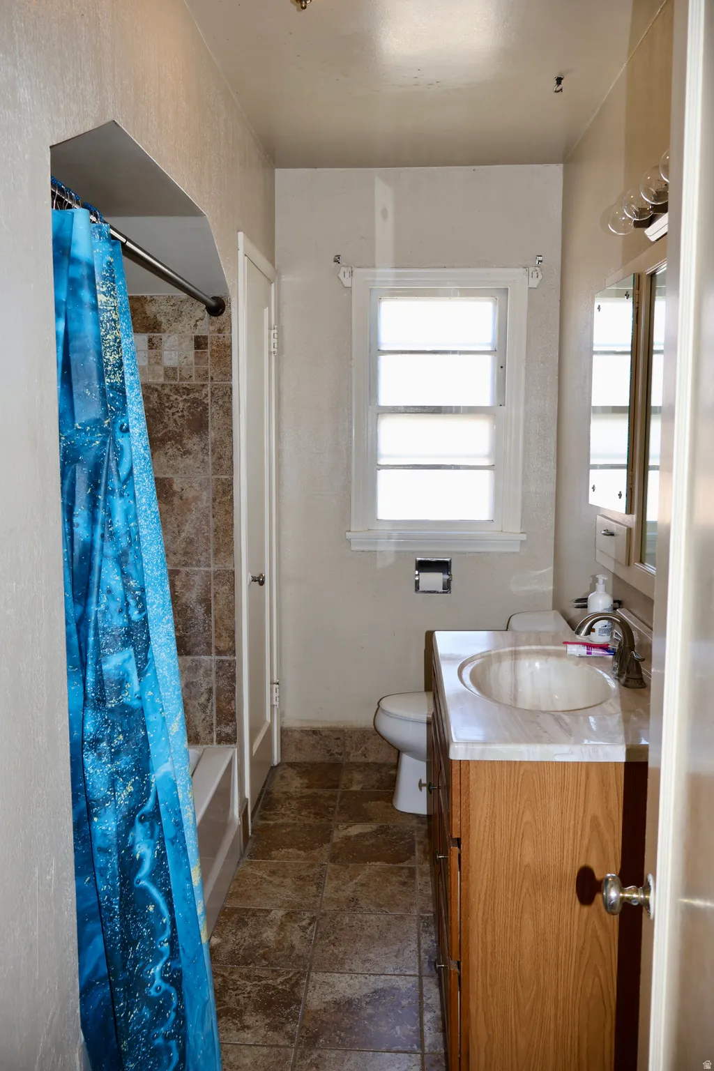 Bathroom featuring a tub/shower combination with mosaic tile surround, vanity with an integrated sink and light wood-finish cabinetry, and a window with white trim
