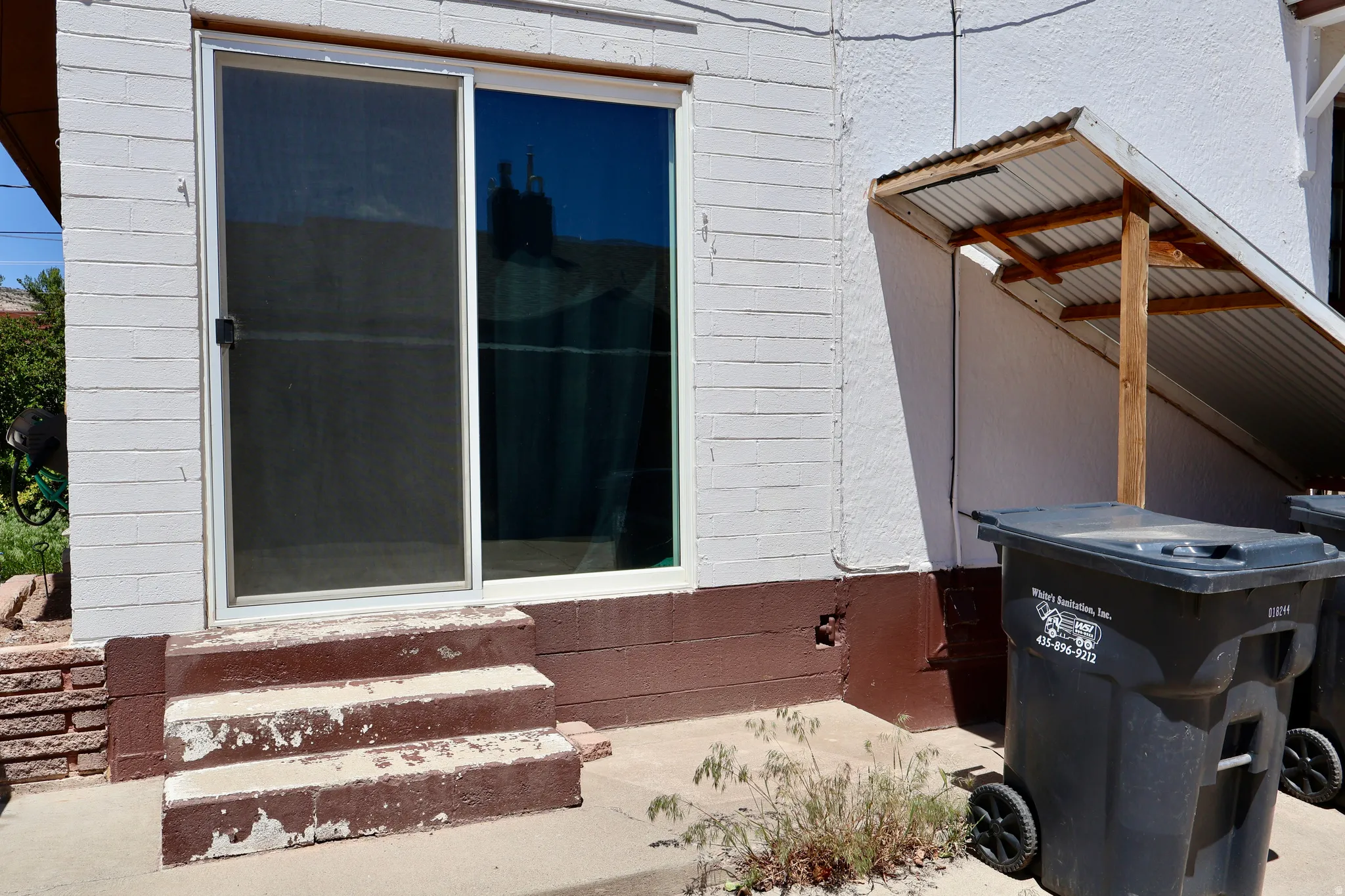 Sliding glass door with screen, accompanied by exterior brickwork and an attached wood-framed awning with a corrugated metal roof