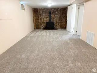 Spacious room featuring new carpeting, a stone-accented wall, and a black wood-burning stove and brand new carpet as of June 26