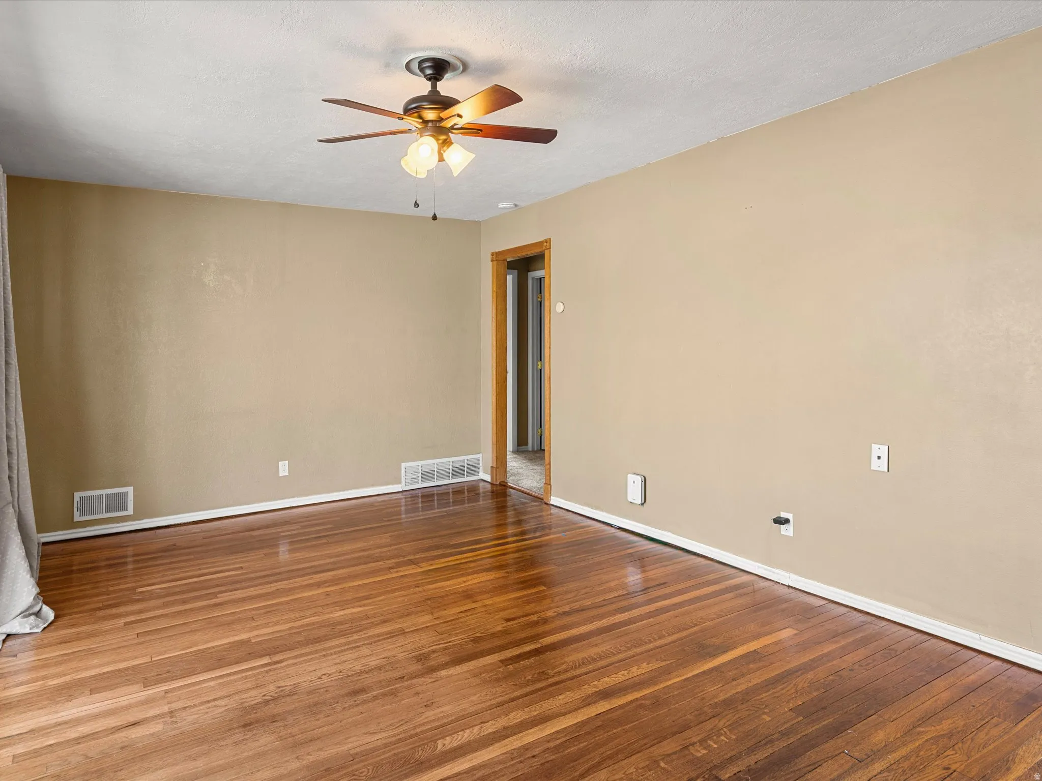 Room featuring rich wood-finish flooring, light tan walls, white baseboards, and a bronze ceiling fan with integrated lighting