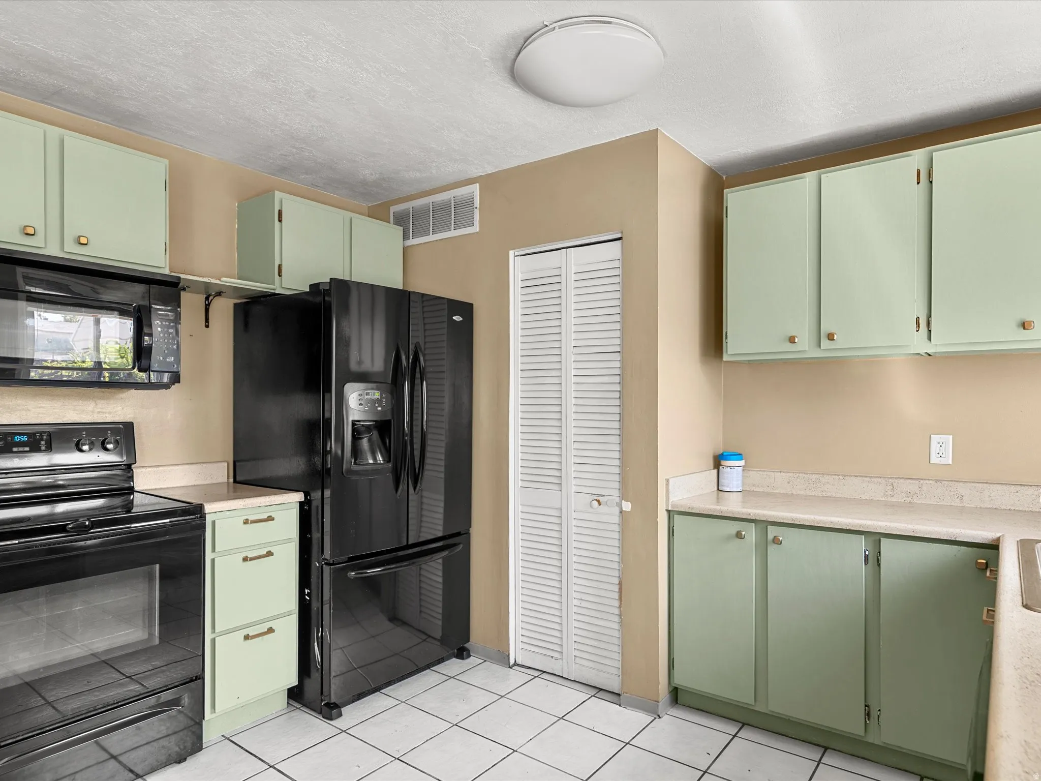 Kitchen featuring light green cabinetry, black appliances including a refrigerator and range, a built-in microwave, and white tile flooring