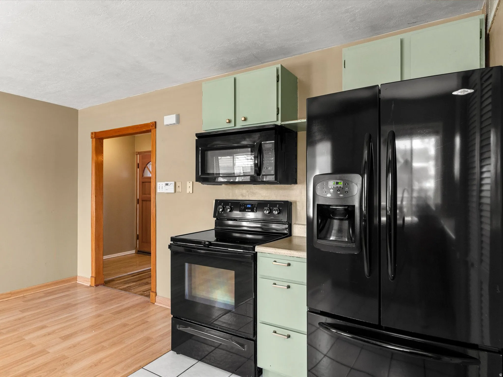 Kitchen featuring black appliances, light green cabinetry, and wood-finish flooring