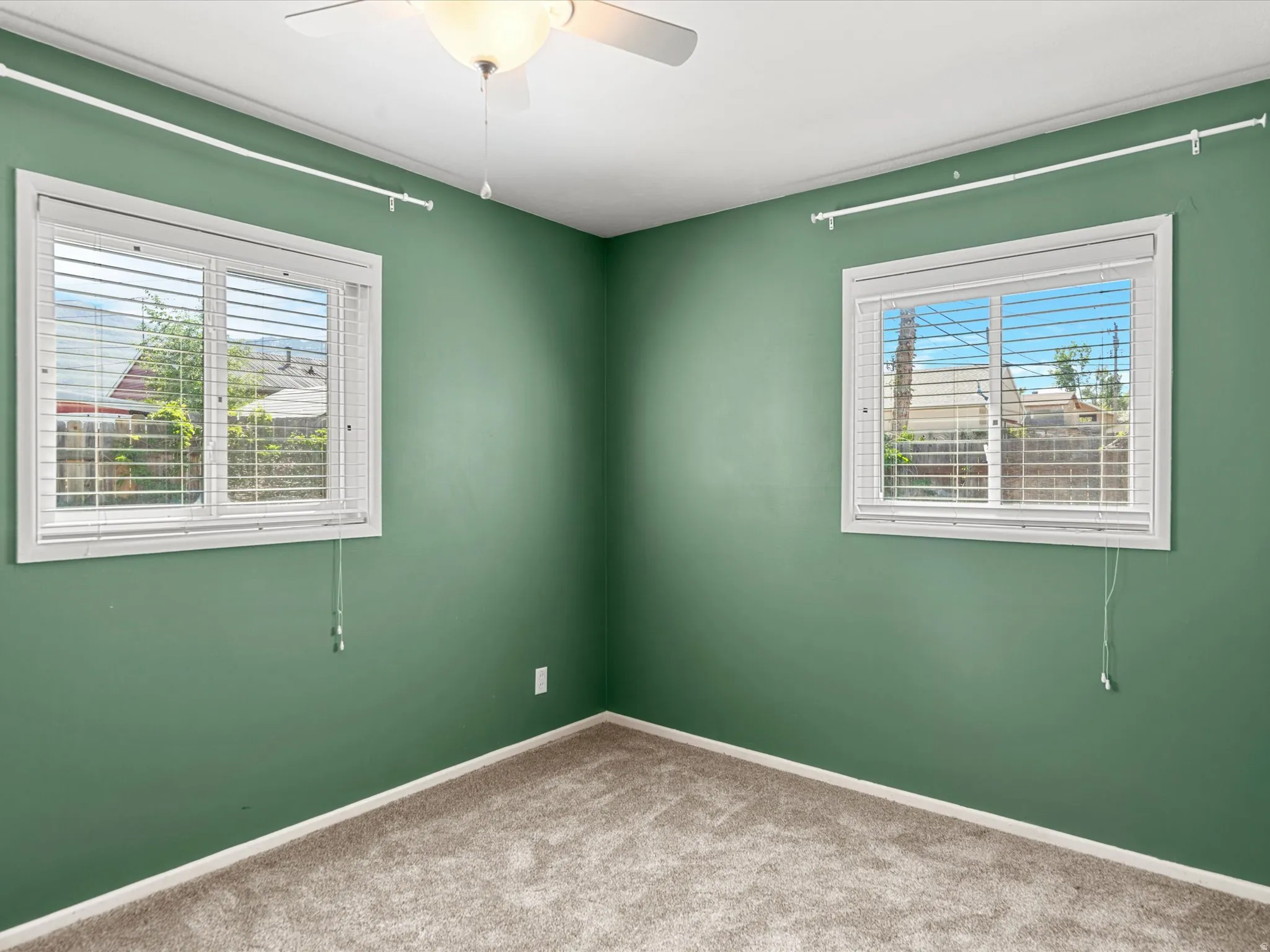 Carpeted interior space featuring two windows with horizontal blinds, a ceiling fan with light fixture, and crown molding