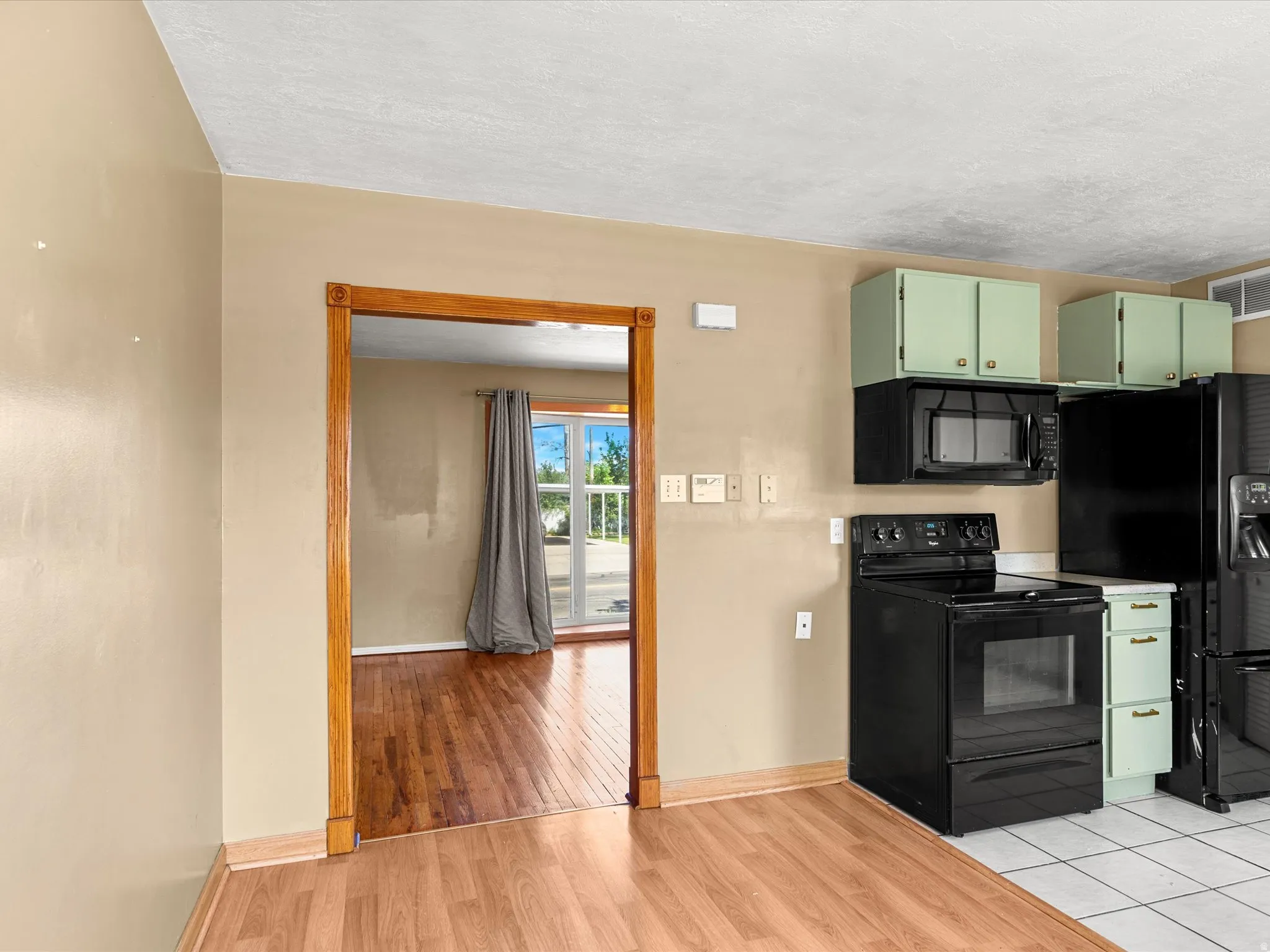 Kitchen featuring light green cabinetry, black appliances, tile flooring, and wood-finish flooring