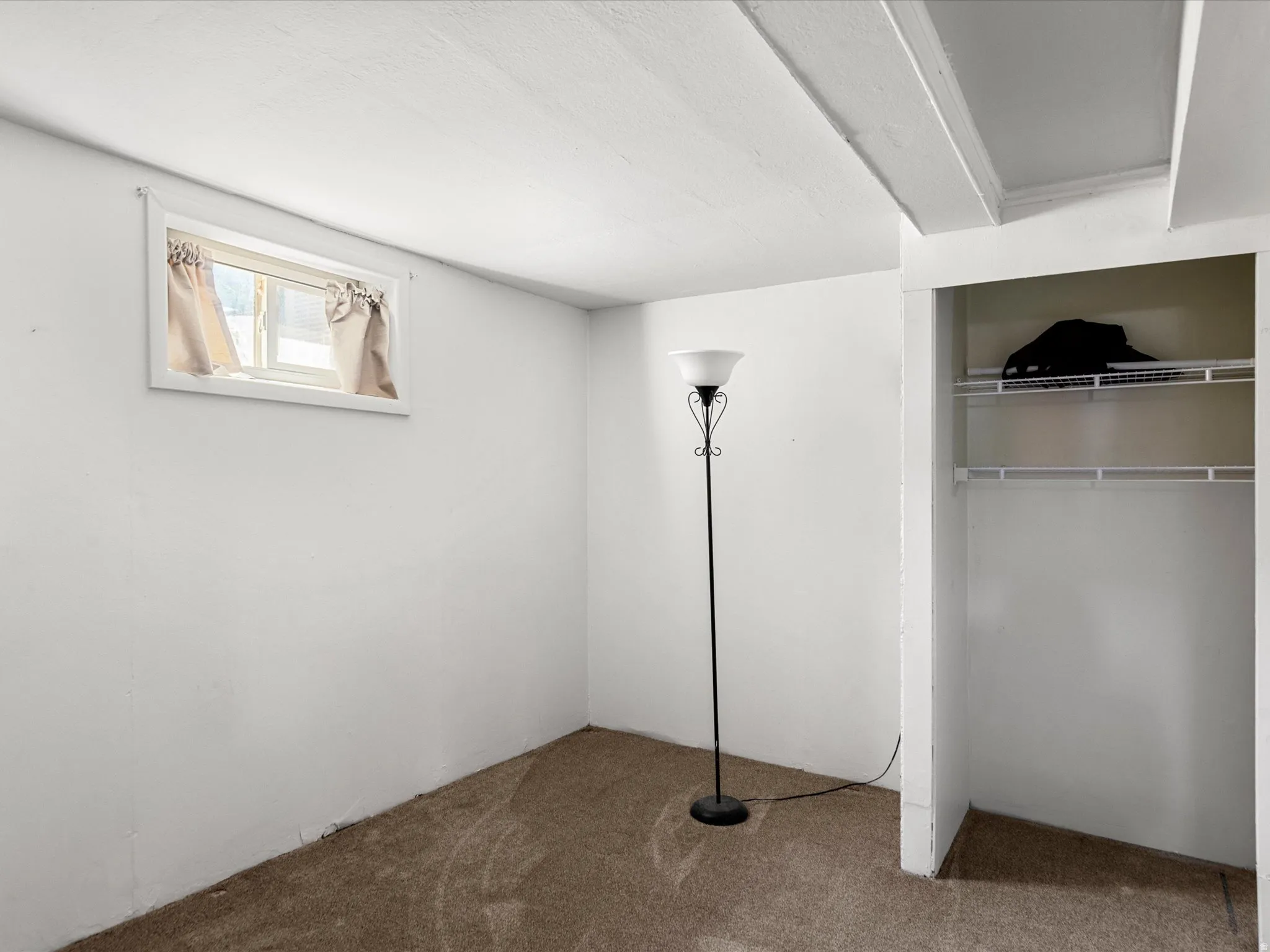 Windowed room featuring white walls and textured carpet flooring