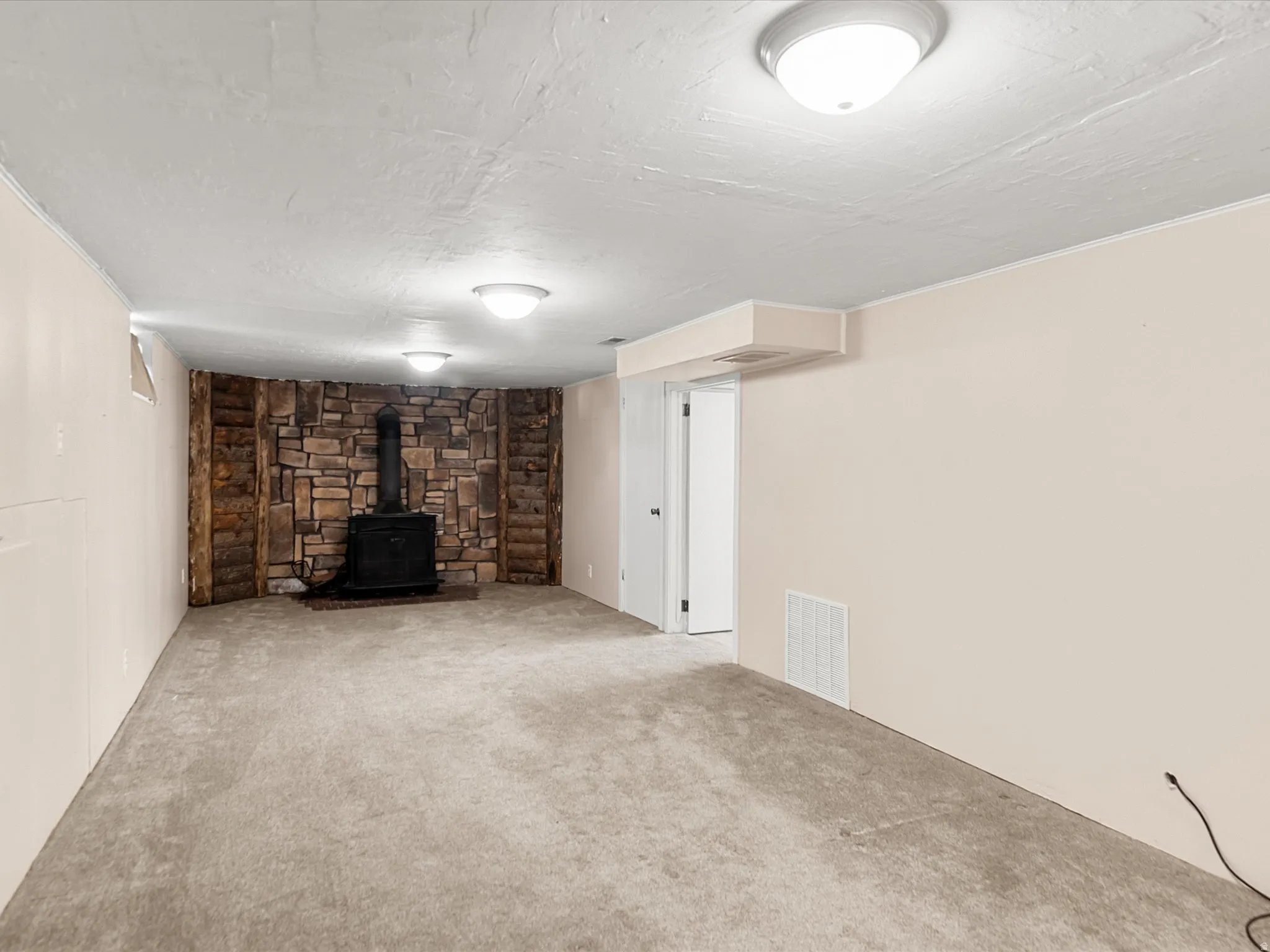 Spacious room featuring neutral carpet flooring and a prominent stone accent wall with a built-in black wood-burning stove