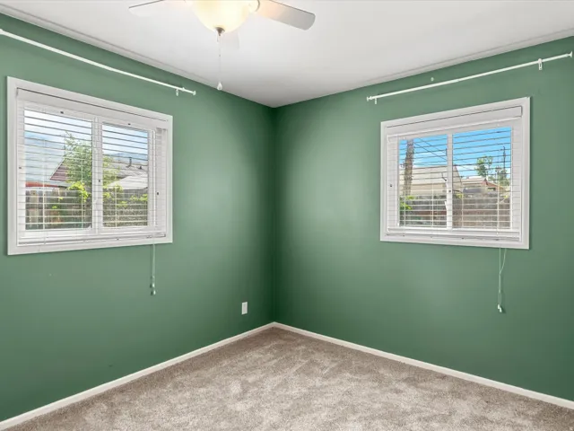 Carpeted interior space featuring two windows with horizontal blinds, a ceiling fan with light fixture, and crown molding
