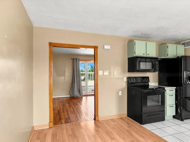 Kitchen featuring light green cabinetry, black appliances, tile flooring, and wood-finish flooring