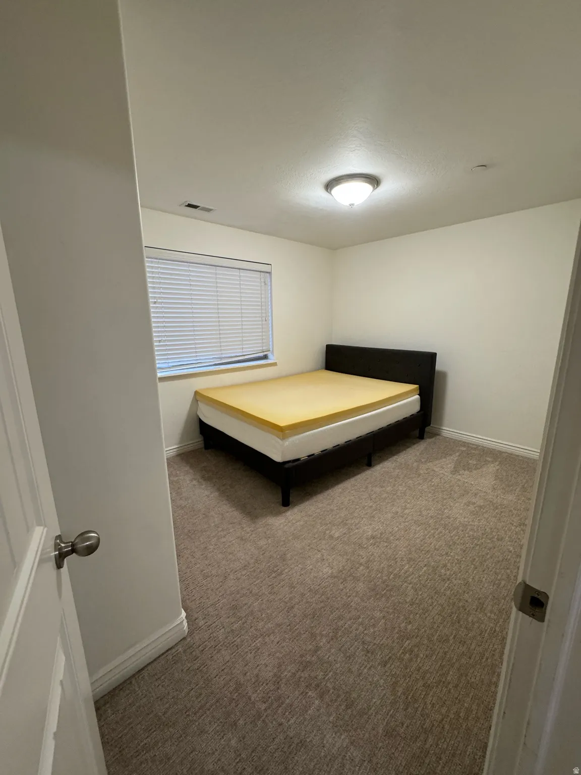 Carpeted room featuring a window with blinds, a ceiling-mounted light fixture, and white baseboards