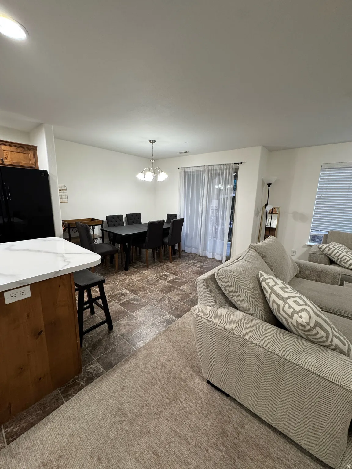 Open-concept living area featuring a kitchen island with a light-toned countertop, wood-finish base cabinetry, and a black built-in refrigerator
