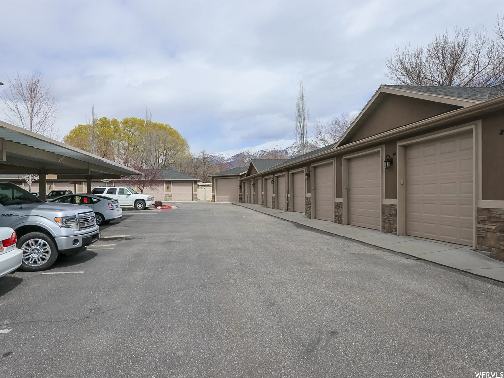 Extensive asphalt parking lot featuring covered parking structures and a row of individual garages with panel doors and stone veneer accents