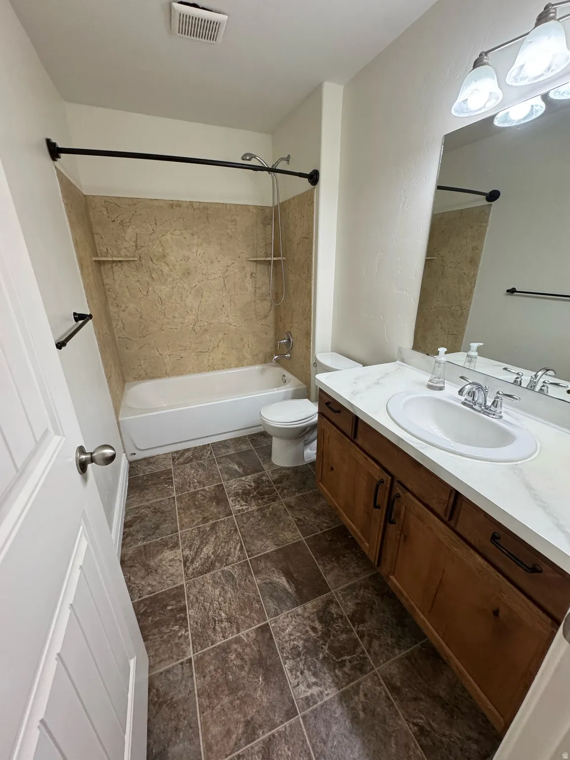 Bathroom featuring a built-in tub with a tiled shower surround, a single vanity with a white countertop and undermount sink, a large wall mirror, and tiled flooring