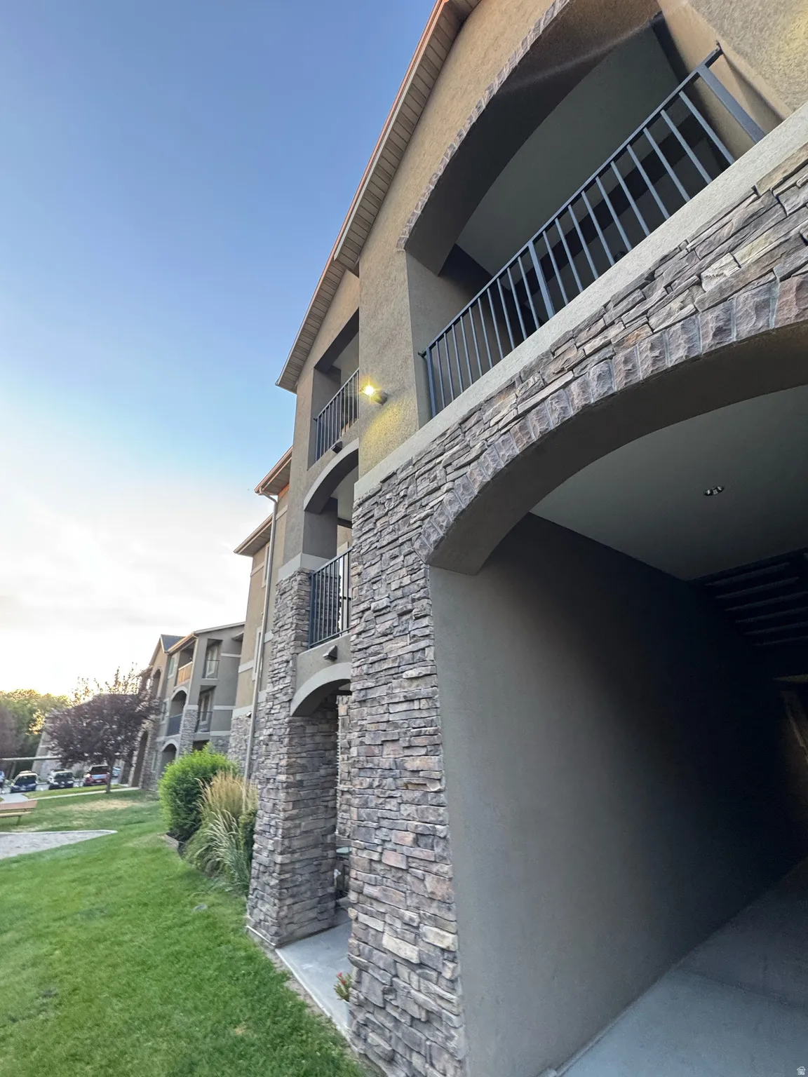 Multi-story building featuring stacked stone accents, stucco exterior, and individual balconies with black metal railings