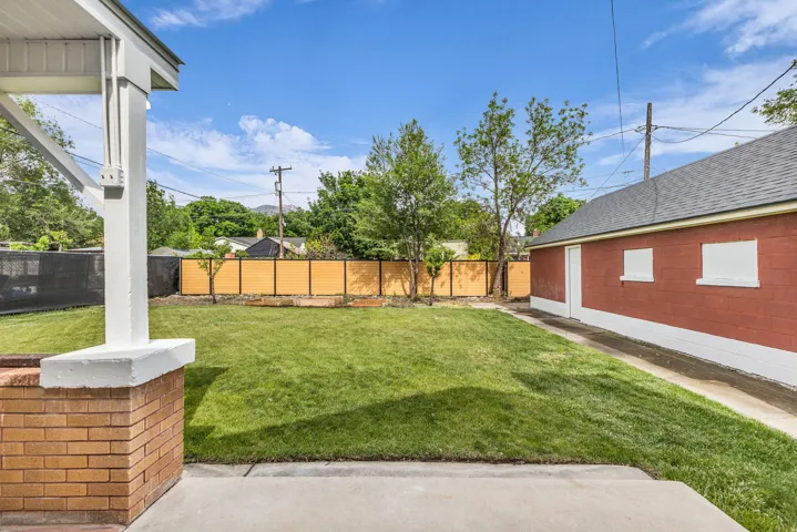 Expansive backyard featuring a manicured lawn, a detached red-brick structure with white accents, and a contemporary horizontal slat fence