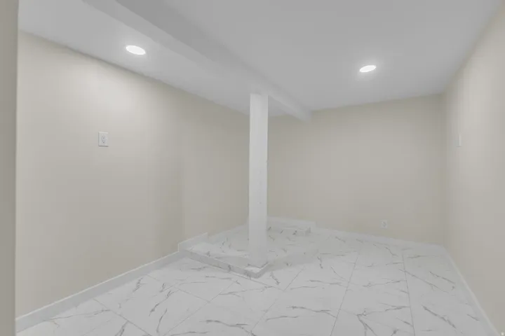 Spacious room featuring light-toned walls, recessed lighting, and white tile flooring with dark veining