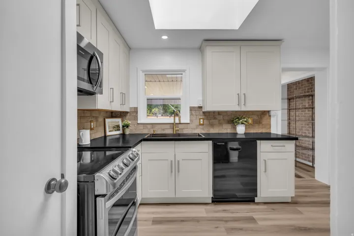Kitchen featuring white shaker cabinetry, black countertops, stainless steel appliances, a tile backsplash, and wood-finish flooring