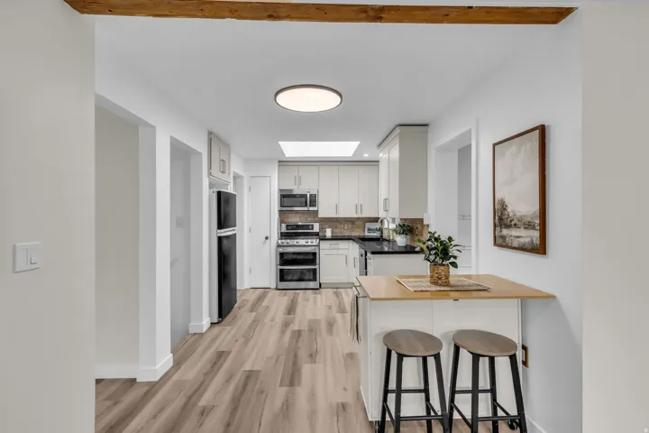 Bright kitchen featuring light wood-finish flooring, white cabinetry, dark countertops, a skylight, and stainless steel appliances