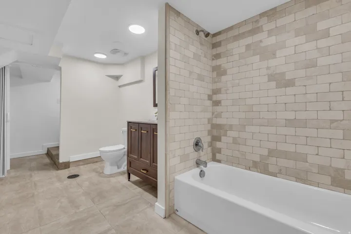 Bathroom featuring a full-size bathtub with subway tile surround, a dark wood-finish vanity with a mounted sink, and recessed ceiling lighting