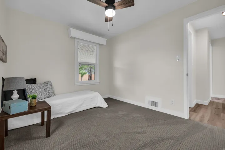 Neutral-toned room featuring a window with exterior views, dark gray carpeting, and a ceiling fan with integrated lighting