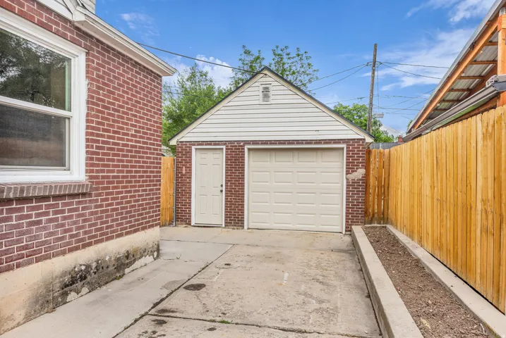 Detached garage with white siding and a brick base, featuring a single garage door and an entry door