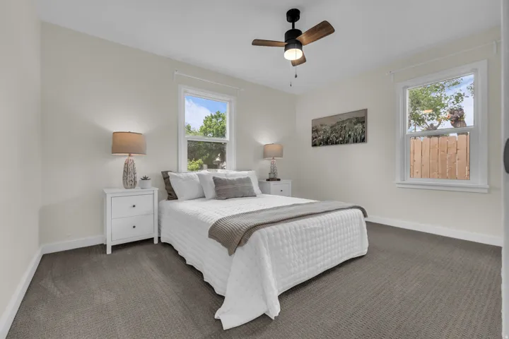 Carpeted room with a ceiling fan, two windows featuring white trim, and light-toned walls
