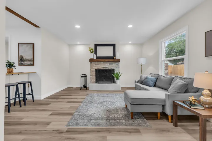 Living area featuring a stone-faced fireplace with a wood mantel, wood-finish flooring, recessed lighting, and a white framed window