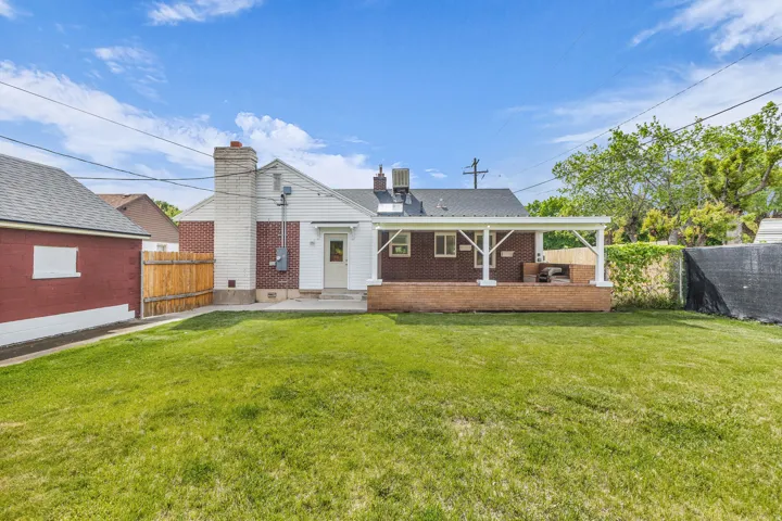 Expansive green lawn with a detached red structure, wooden privacy fencing, and a covered back patio