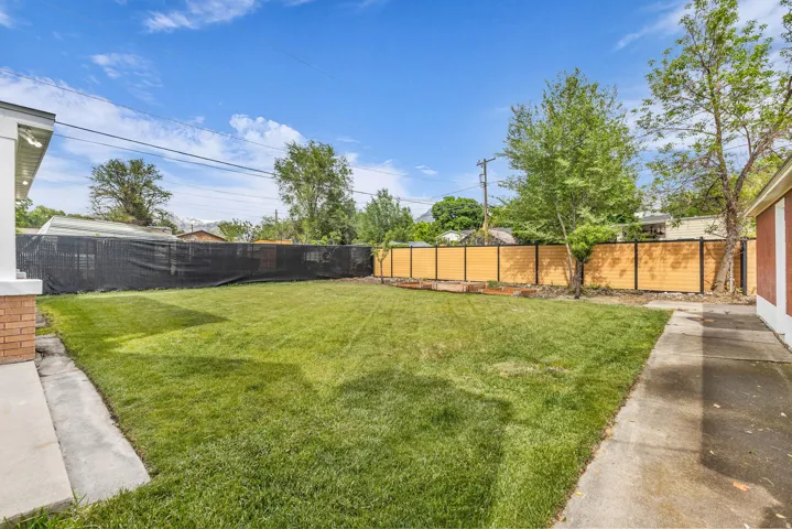Expansive backyard featuring a manicured lawn, established trees, and perimeter fencing