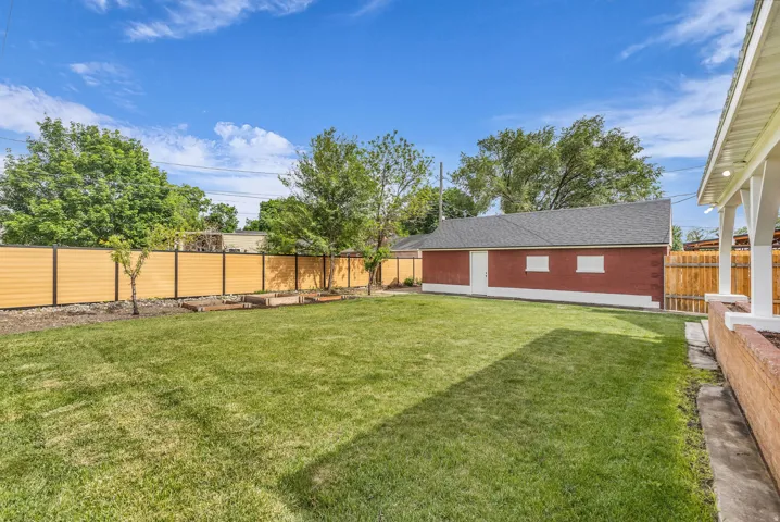Expansive backyard featuring a manicured lawn, a detached brick structure with a shingle roof, a privacy fence with horizontal panels, and raised garden beds