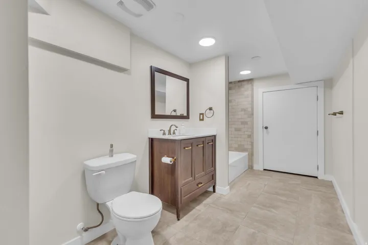 Bathroom featuring a wood-finish vanity with a white countertop and rectangular sink, a framed mirror, and recessed lighting