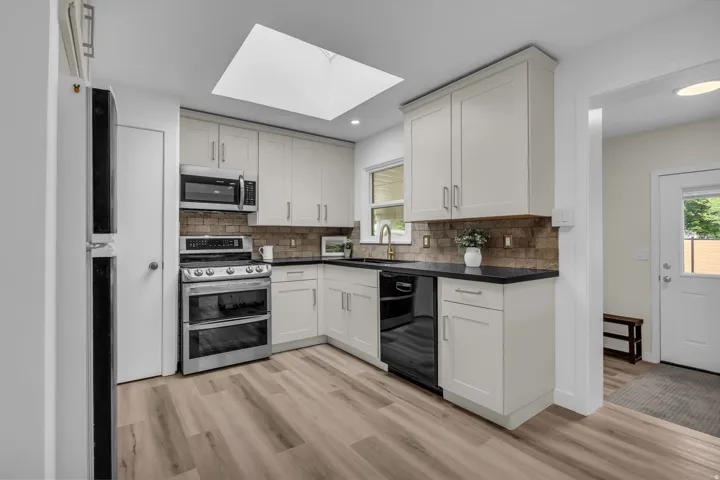 Modern kitchen featuring light cabinetry, dark countertops, a tile backsplash, stainless steel appliances, and wood-finish flooring