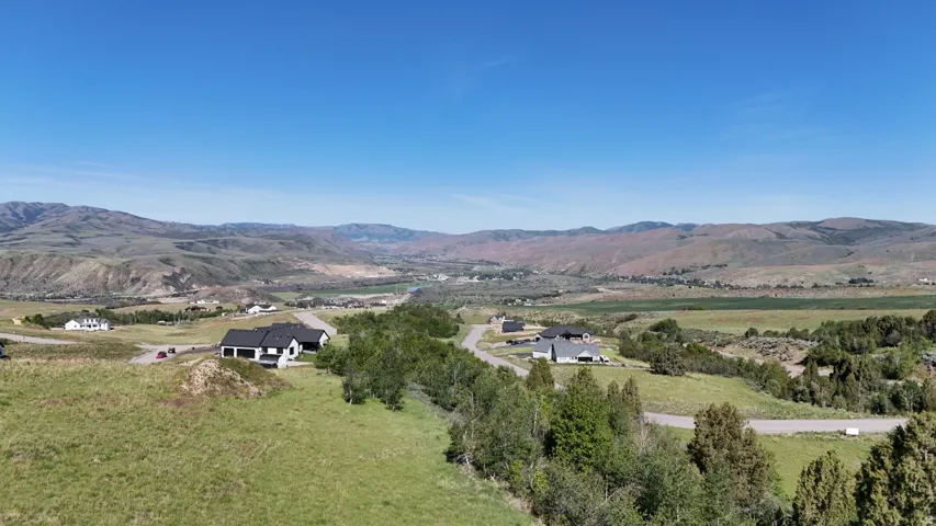 Expansive high-elevation property featuring a contemporary residence with a black roof and white siding, surrounded by rolling hills and distant mountainous terrain