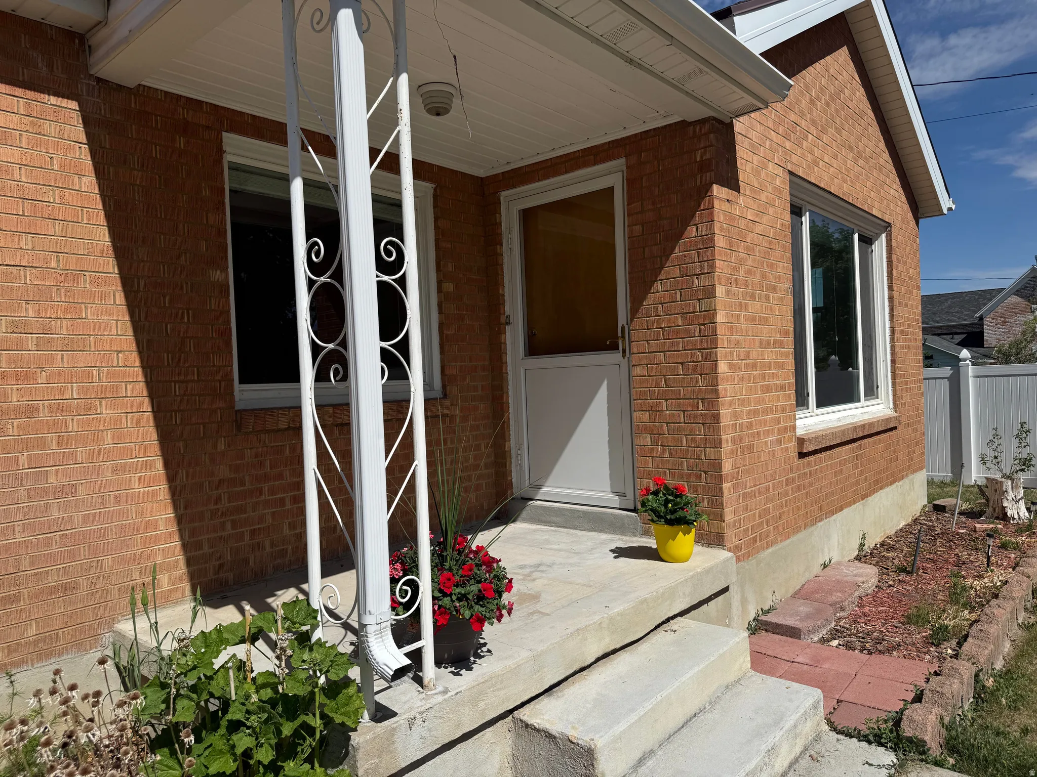 Brick exterior featuring white trim, a covered entry, concrete steps, and a white storm door
